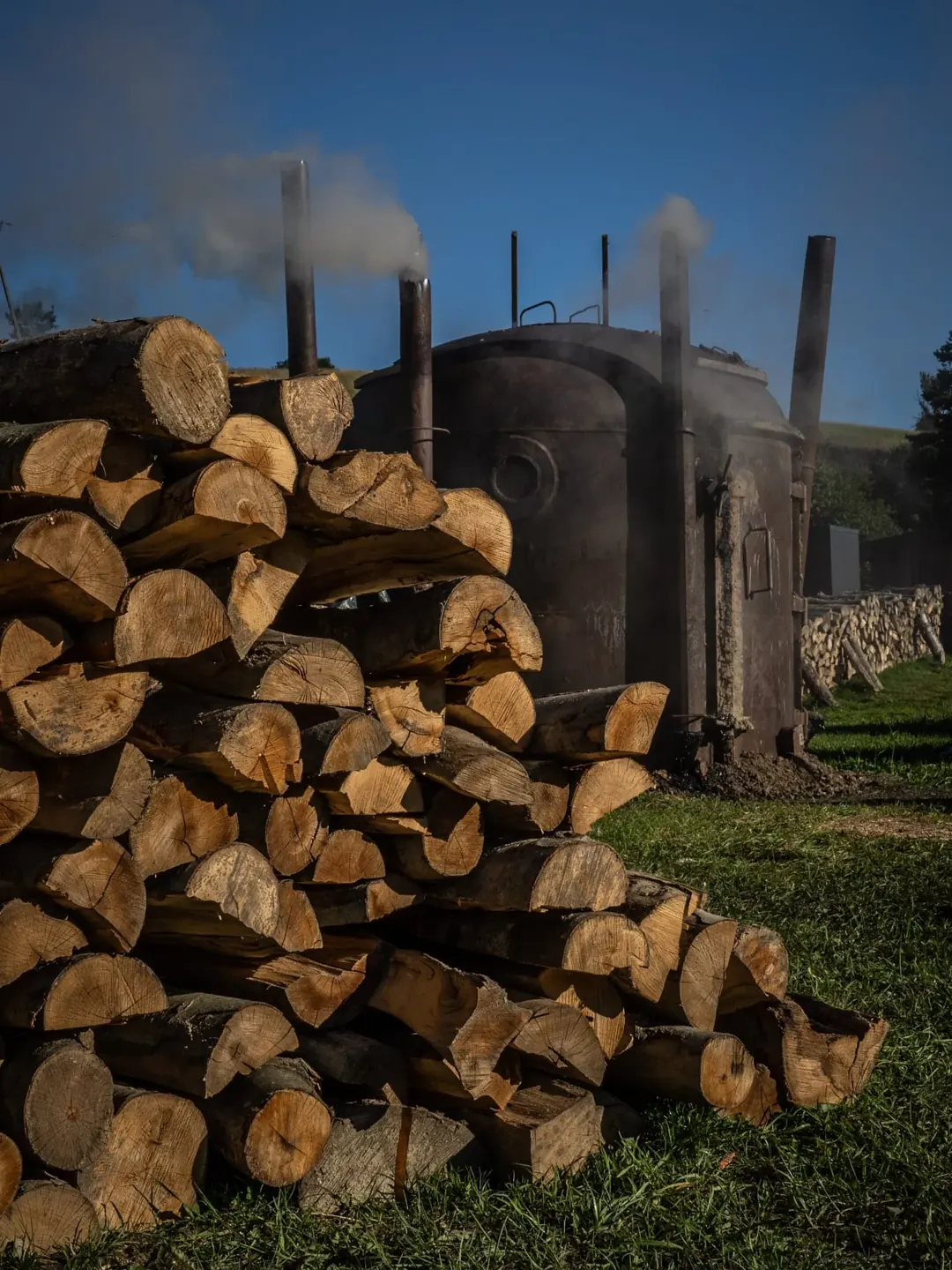 Holzstapel vor den rauchenden Verkohlungsmeilern